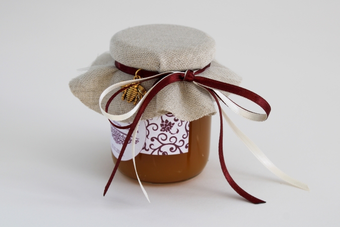 Medus dāvanu burciņa ar zelta krāsas bitīti un atlasa lenšu pušķi.